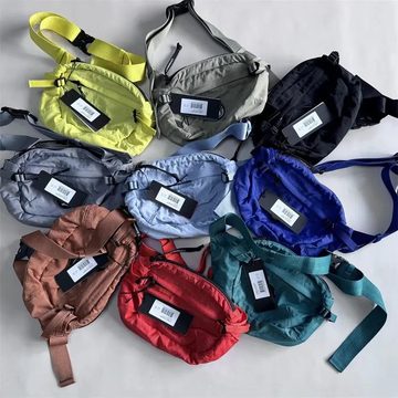Pile of nylon belt bags in lime, grey, navy, rust, red and teal with tags