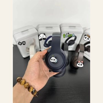 Hand holding navy over-ear headphones with a panda motif, boxes behind