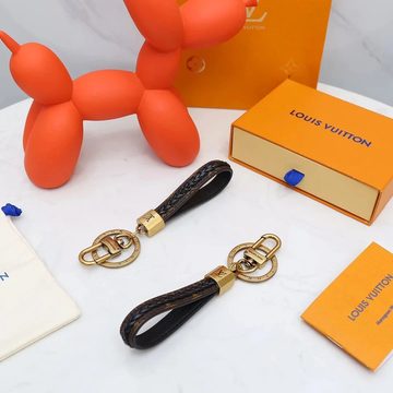 Two brown braided loop key rings with gold rings beside an orange balloon-dog figure