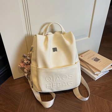 Cream faux-leather backpack with a drawstring top and embossed lettering on the front, standing on a sofa
