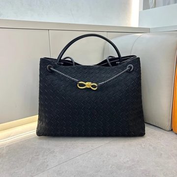 Black woven tote bag with rounded handles and a gold knot clasp, on a white bench