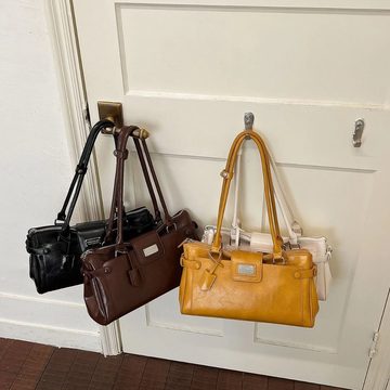 Three baguette-shaped shoulder bags in black, brown and mustard hanging on a door